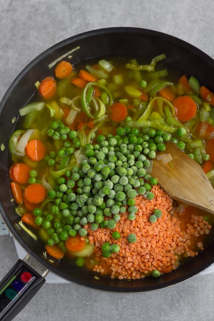 large frying pan with sauteed vegetables, lentils, peas and vegetable stock