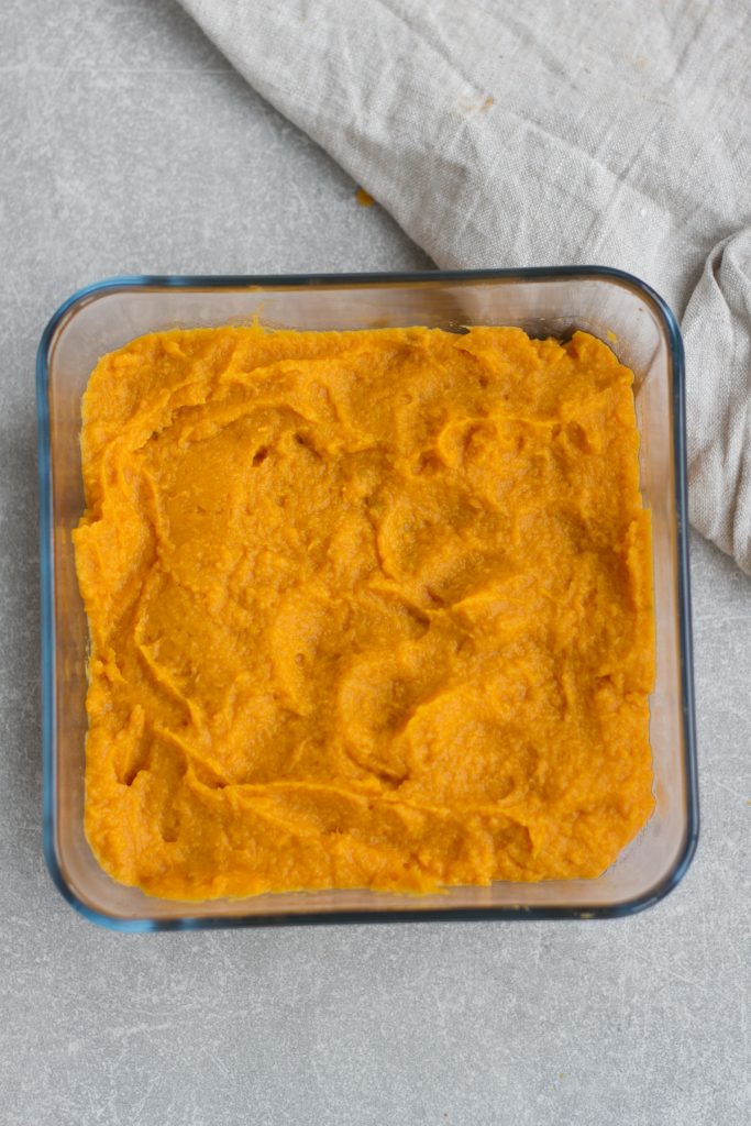 vegan lentil shepherds pie filling in a glass tupperware container topped with mashed sweet potato